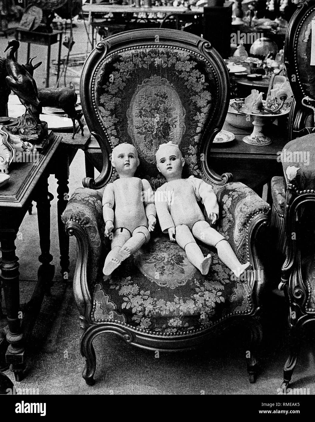 Due antiche bambole di porcellana sedersi in una vecchia poltrona di un mercato delle pulci, chiamato anche "arche aux puces', a Parigi. Foto Stock