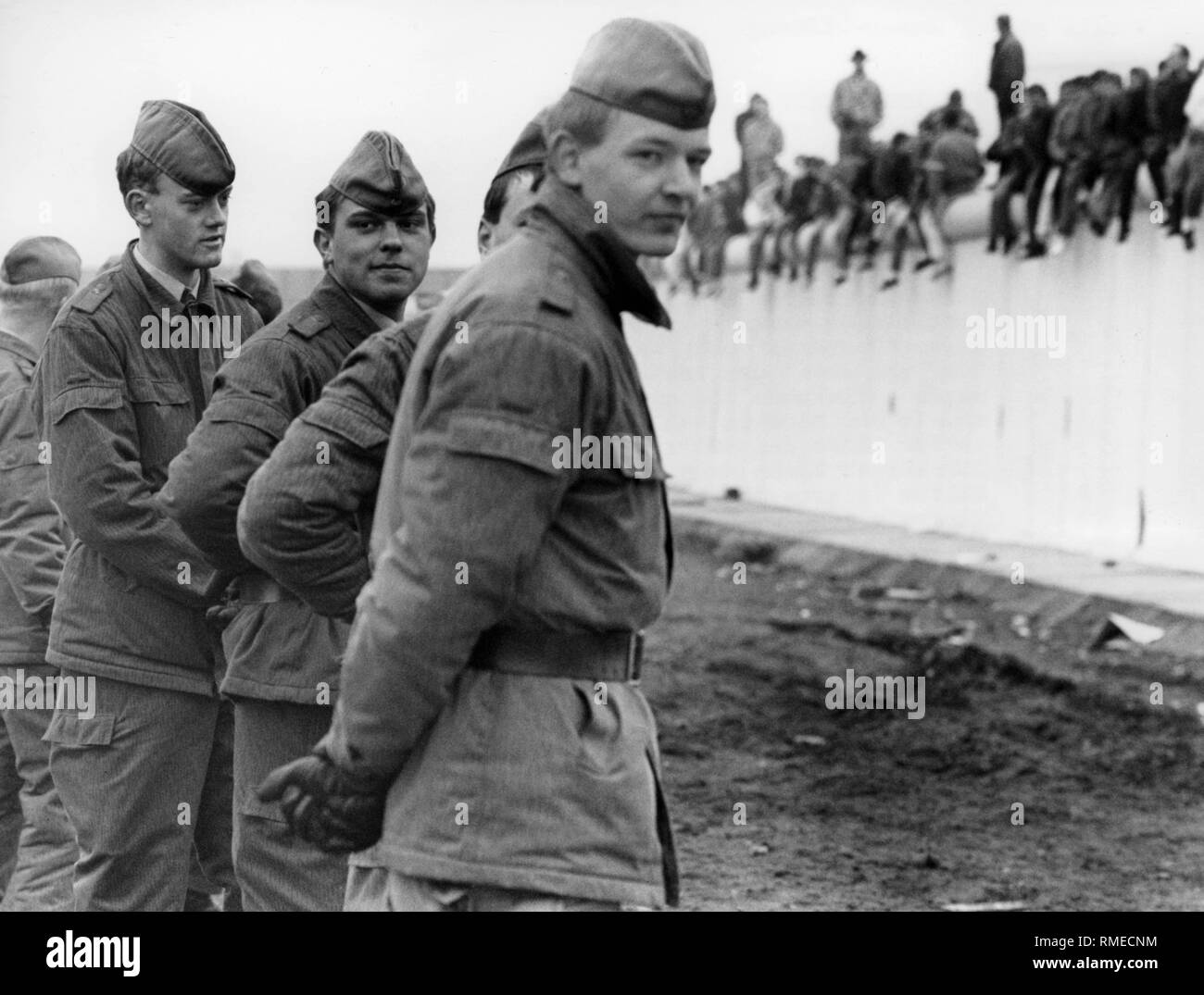 I membri delle truppe di frontiera vis-a-vis gente seduta sul muro di Berlino. Foto Stock