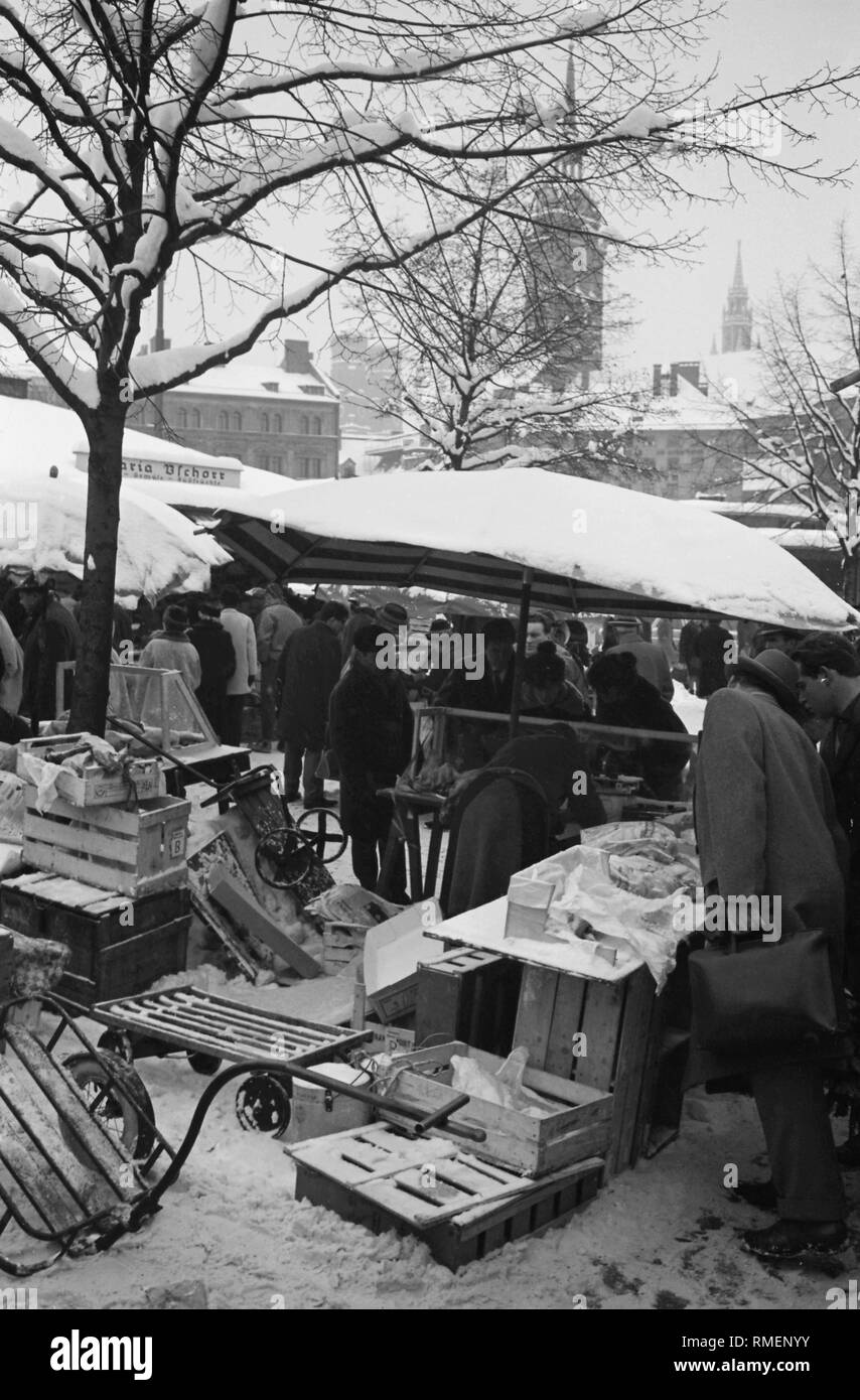 Pressione di stallo di mercato a Monaco di Baviera Viktualienmarkt in inverno. Sullo sfondo le torri della chiesa di San Pietro e della Chiesa dello Spirito Santo. Foto Stock