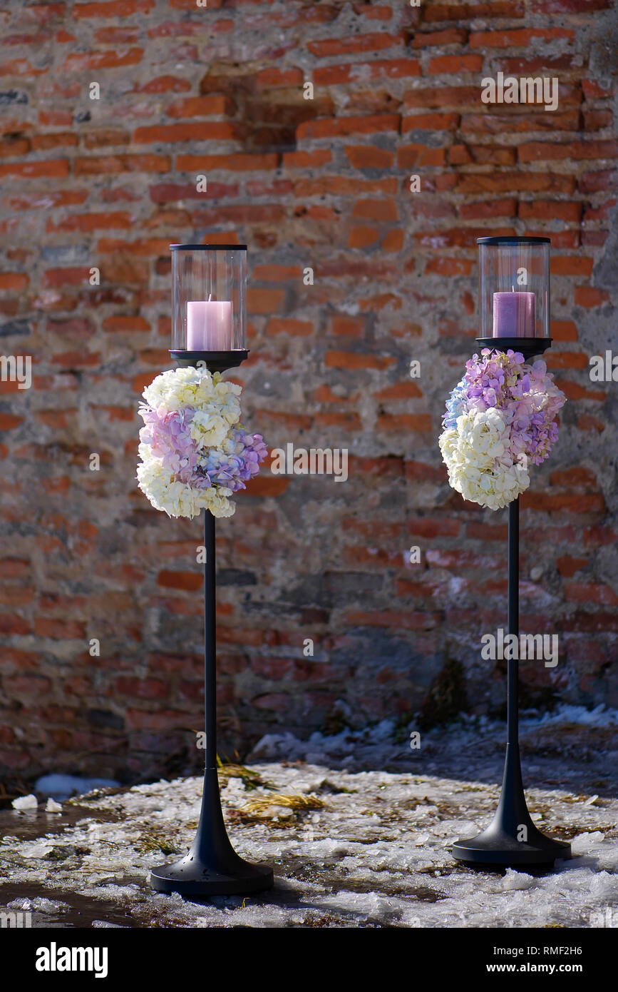Due esterni free-standing portacandele con colori pastello e ortensie mazzi alla base, elemento decorativo per un evento formale o un matrimonio Foto Stock