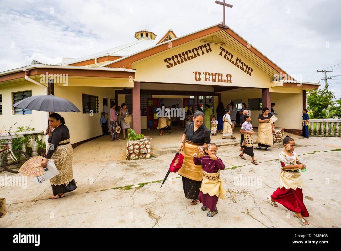 Parrocchiani Polinesiano nel tradizionale abito Tongan a piedi al di fuori della Chiesa Cattolica come messa finisce, Pangai village, Ha'apal Gruppo in Tonga, Polinesia. Foto Stock