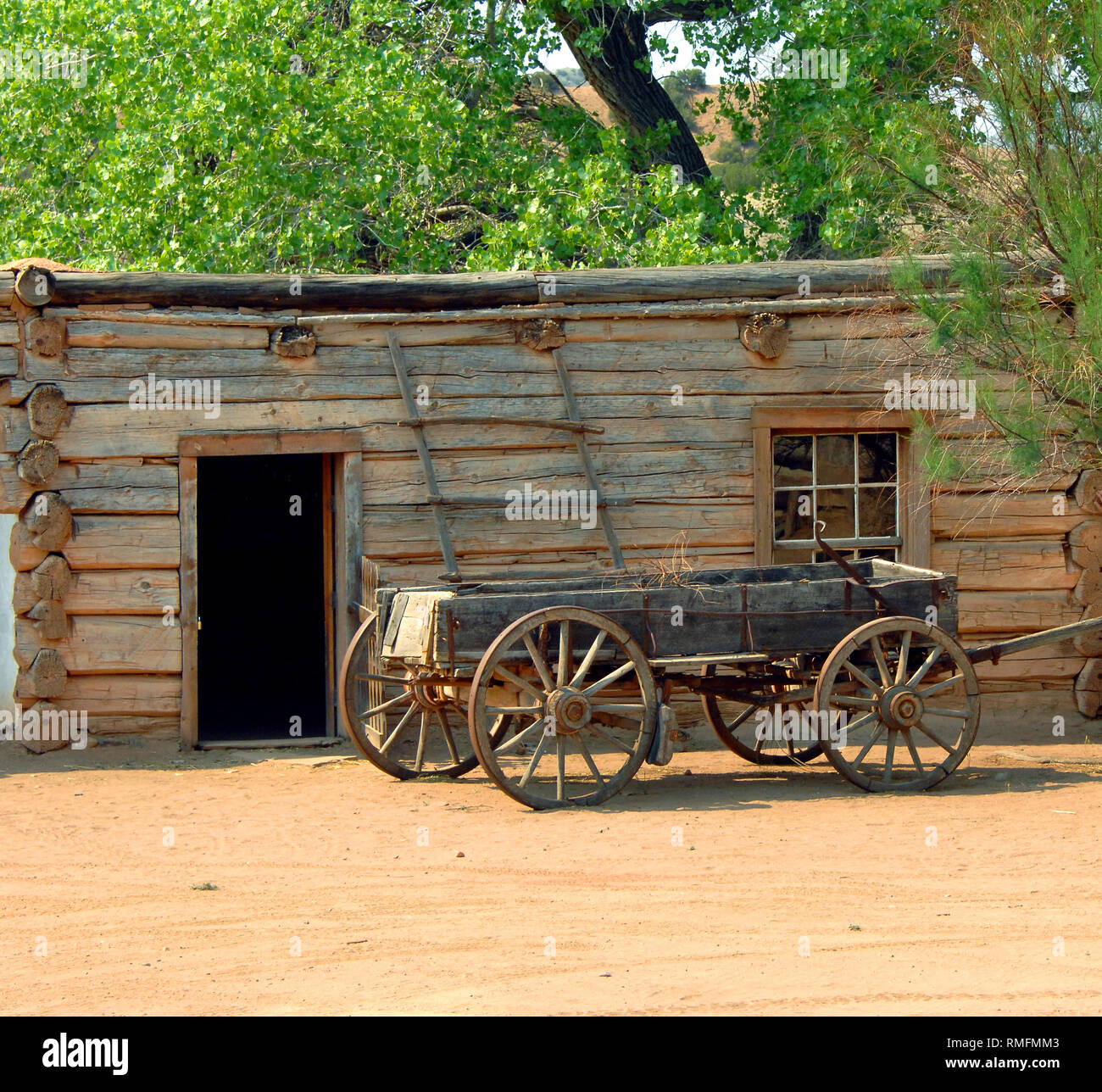 Legno vecchio carro è parcheggiato su un vicolo polveroso al di fuori di un Log Cabin. La scala in legno si appoggia contro l'edificio. Foto Stock