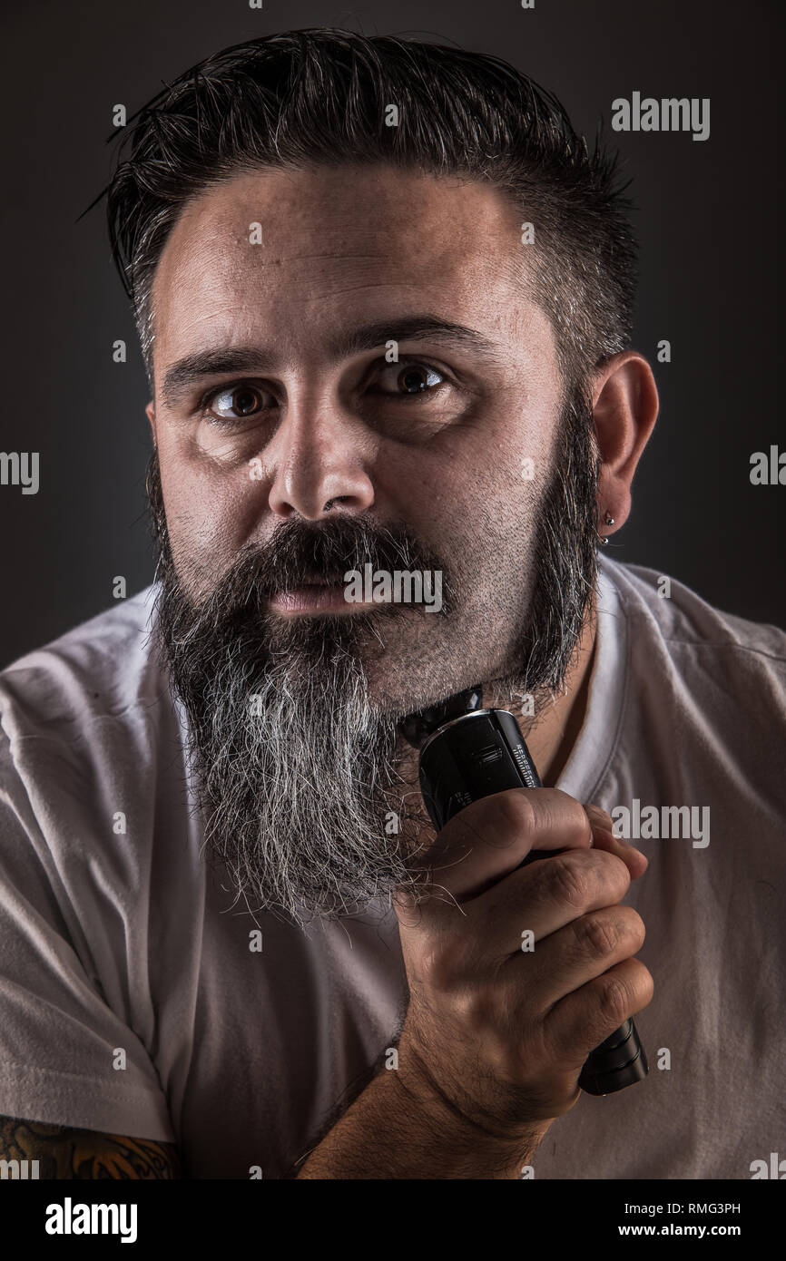 Bel maschio adulto con rasoio elettrico di radersi la barba e guardando la  telecamera mentre in piedi su sfondo grigio Foto stock - Alamy