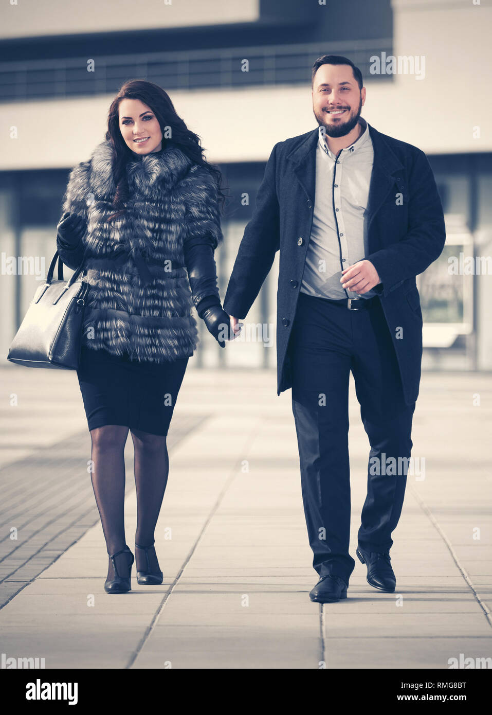 Felice moda giovane coppia in amore a camminare su una strada di città elegante alla moda uomo nel classico mantello nero e la donna che indossa la pelliccia di volpe camicia Foto Stock