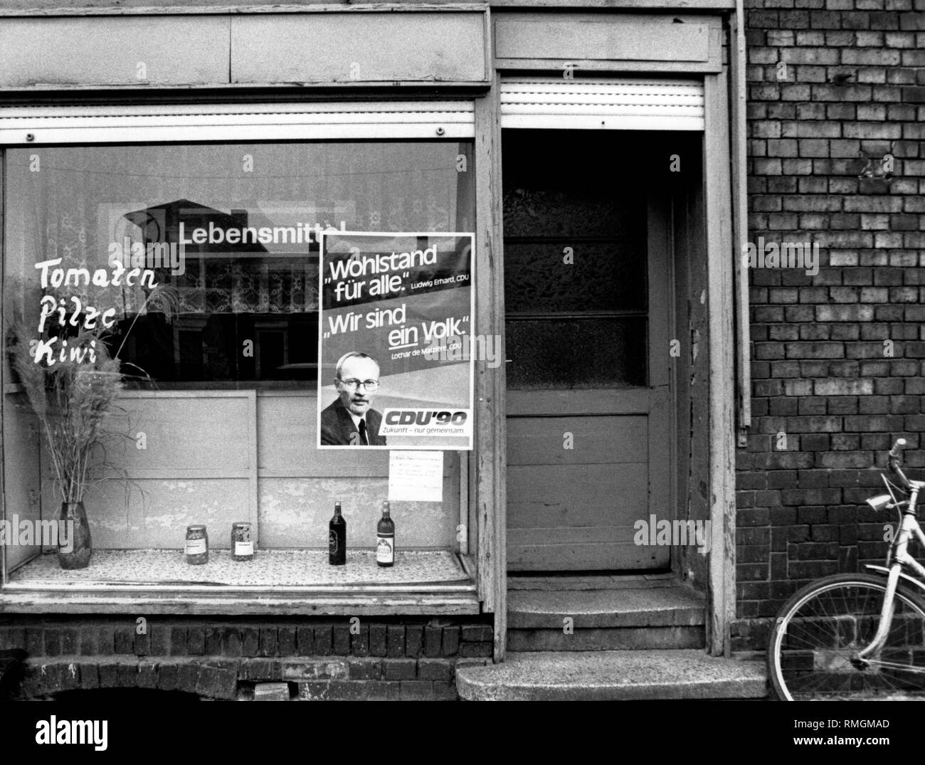 Un cartellone elettorale della CDU con un ritratto di Lothar de Maiziere e i corsi 'Wohlstand fuer alle' (prosperità per tutti) e "Wir sind ein Volk' ('siamo una nazione') da Ludwig Erhard e Lothar de Maiziere decora la vetrina di un negozio di alimentari in Bitterfeld. Foto Stock
