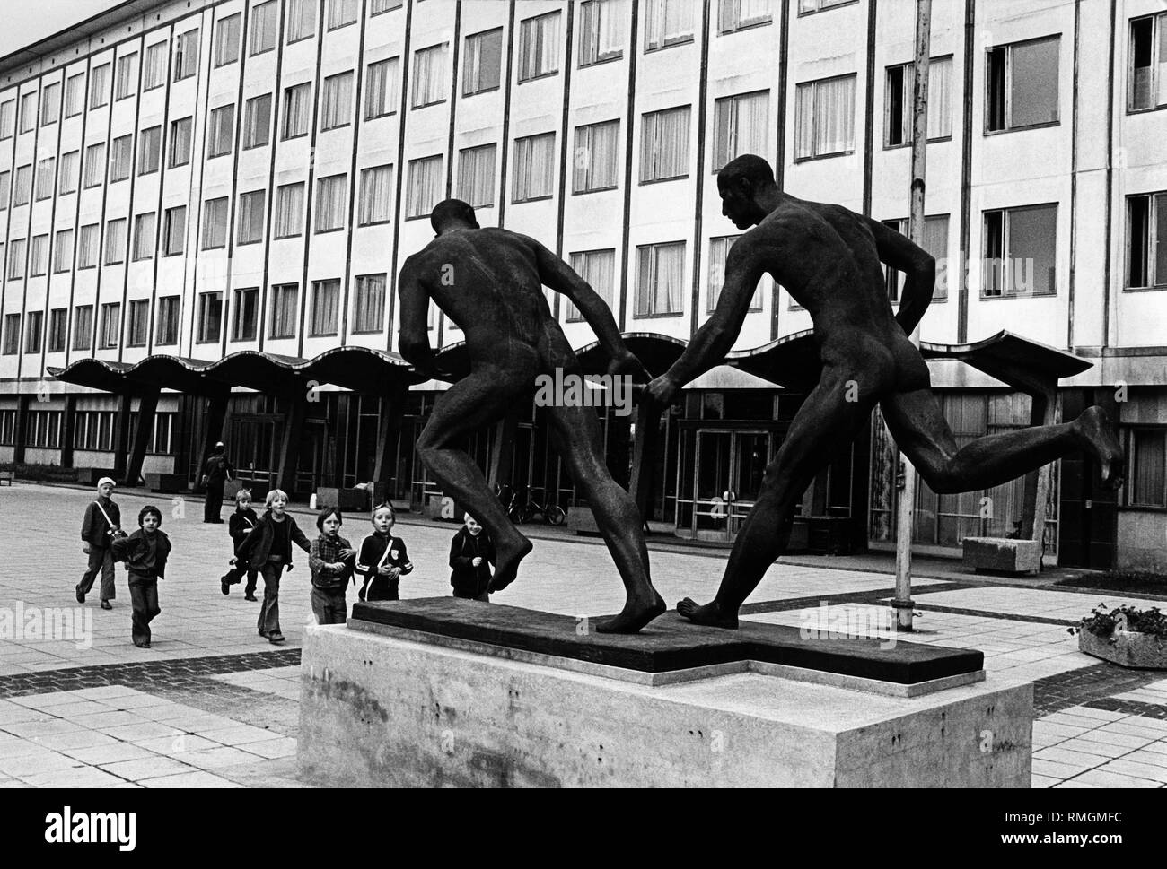 Presso la piazza di fronte al DHfK in Leipzig in una materia plastica è stato impostato. La scultura mostra due guide di relè, uno di loro mani il testimone all'altro. I bambini stanno guardando le opere d'arte. Arte in architettura. Foto Stock