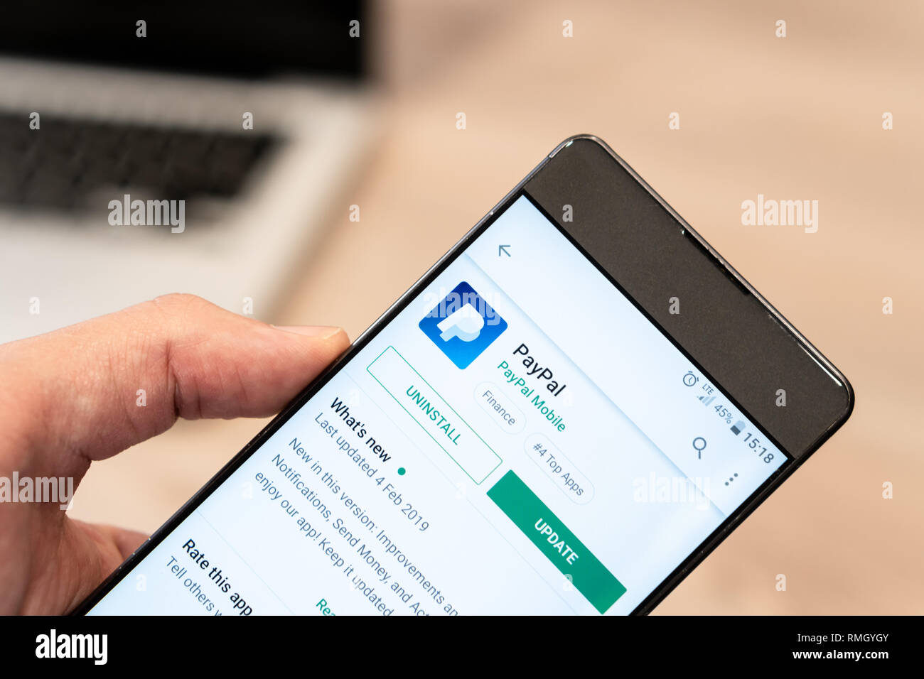 Mano umana tenendo il telefono cellulare - paypal app su app store, computer laptop in background. La Slovenia 13.02.2019 Foto Stock