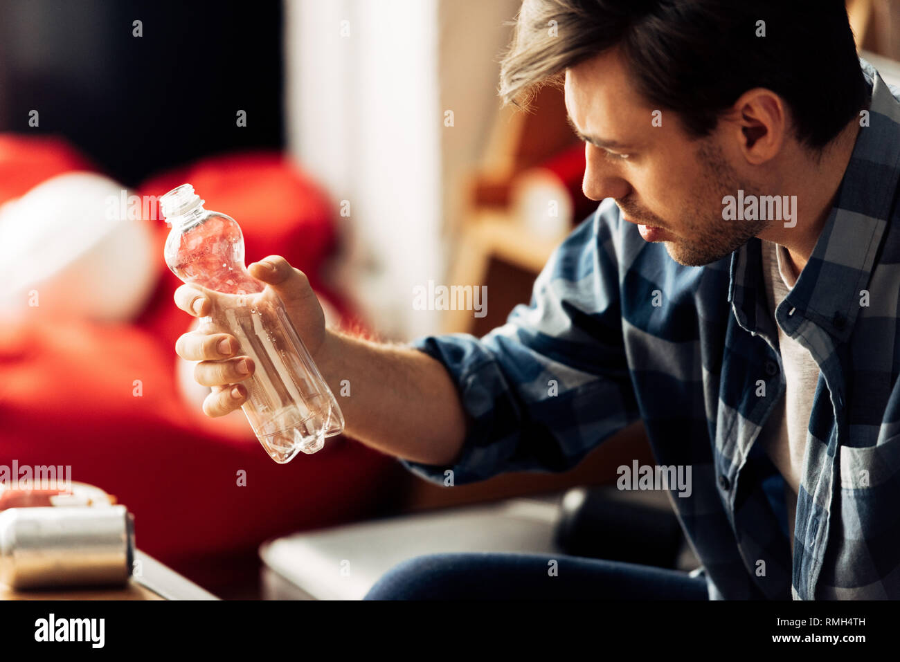 L'uomo soffre di sbornia guardando una bottiglia con acqua a casa Foto Stock