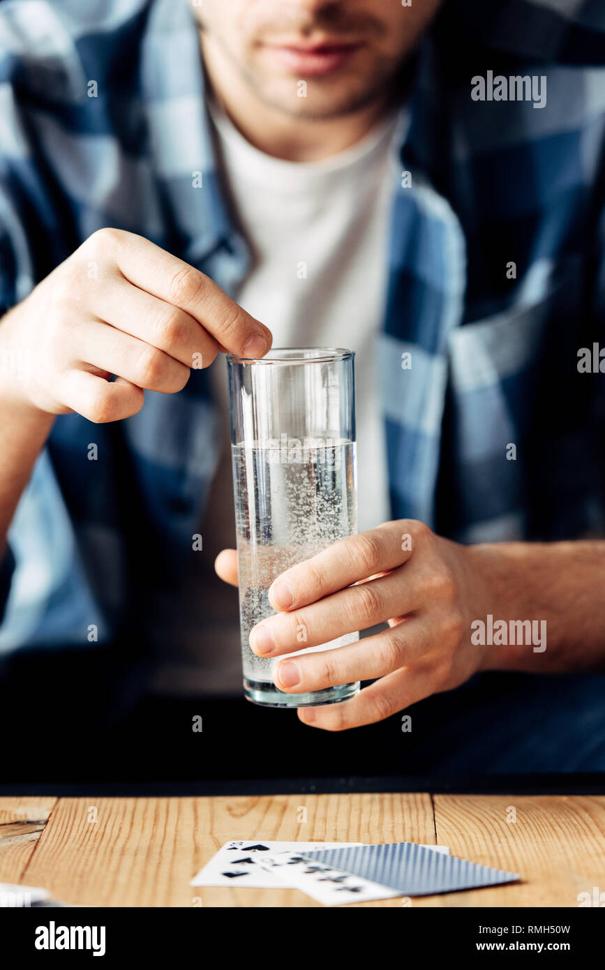 Messa a fuoco selettiva dell uomo che soffre di sbornia tenendo l'aspirina e un bicchiere di acqua in mani Foto Stock
