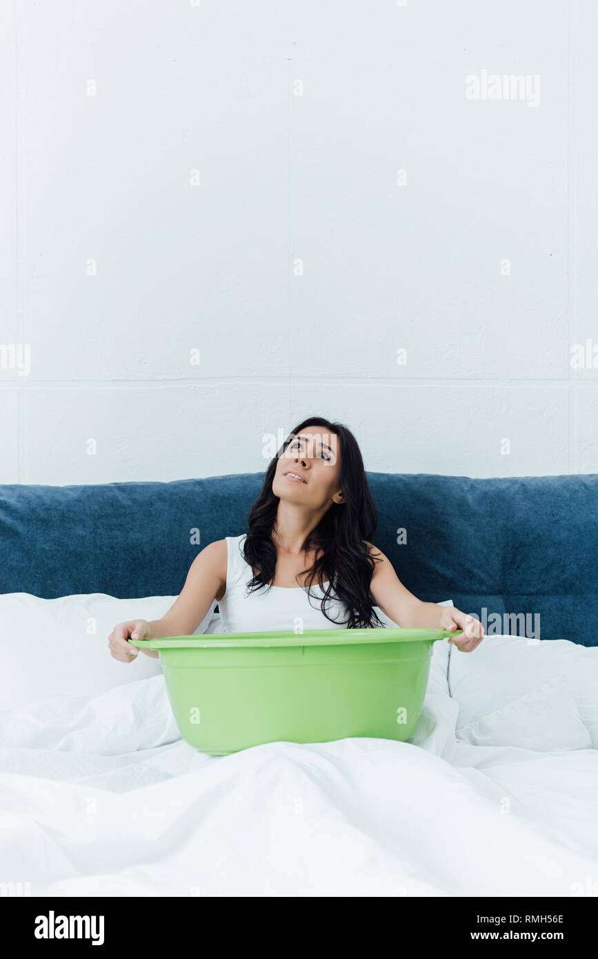Sconvolto brunette donna seduta sul letto e bacino di contenimento Foto Stock