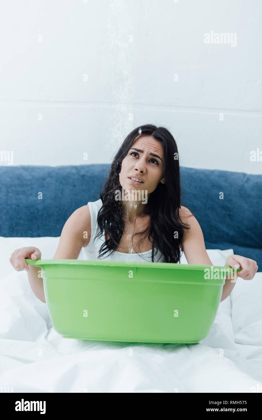 Sconvolto brunette girl holding bacino verde nel letto e guardando in alto Foto Stock