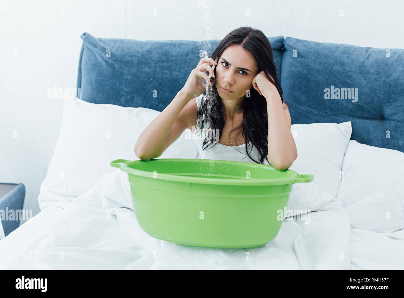Irritato brunette donna parlando sullo smartphone mentre è seduto nel letto con vasca Foto Stock