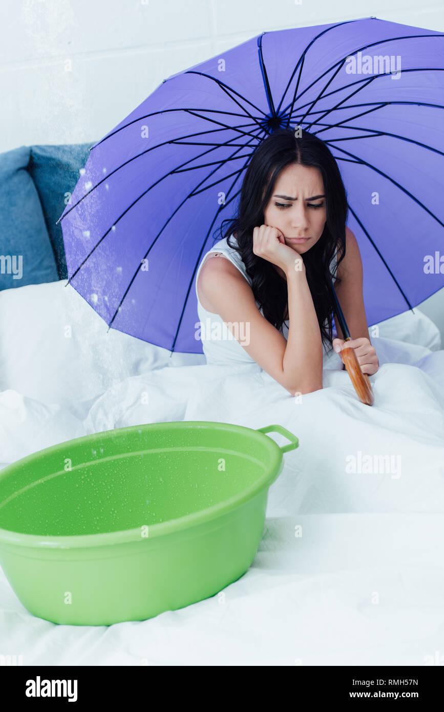 Ragazza triste holding ombrello viola durante la perdita di acqua in camera da letto Foto Stock