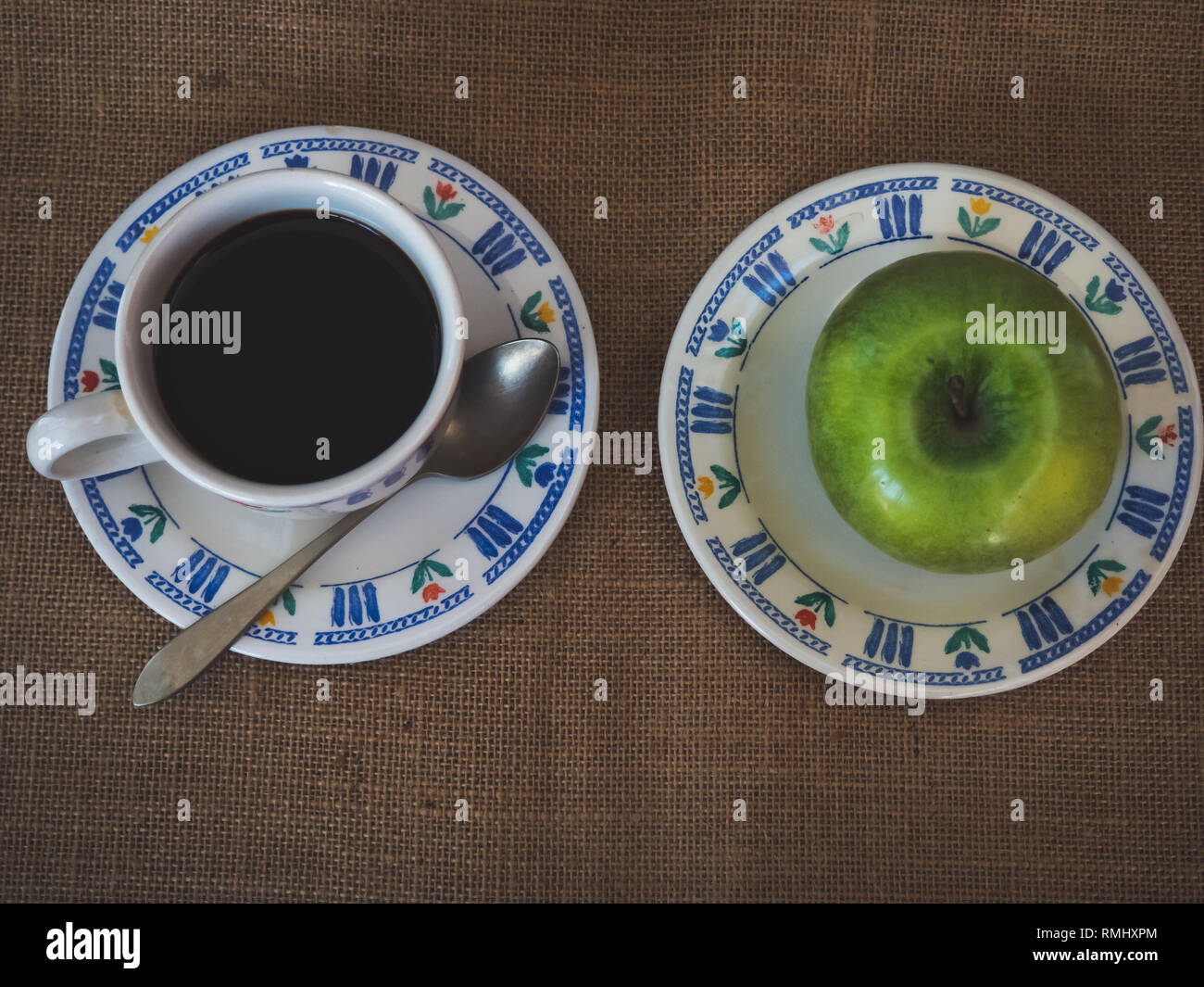 La prima colazione di una tazza in porcellana, un vecchio cucchiaio e una piastra con una mela verde su una tela vintage background Foto Stock