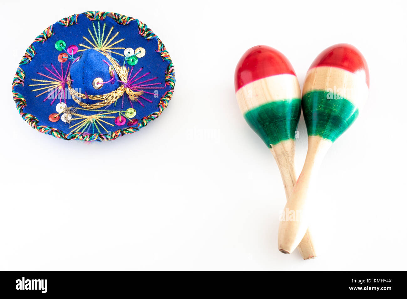 Sombrero blu con ornamenti colorati su sfondo bianco accanto alla coppia di maracas dipinte con i colori della bandiera messicana/Cinco de Mayo concept Foto Stock