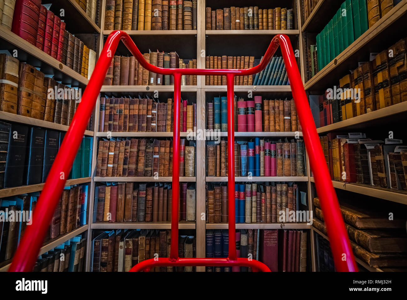 Rochester, Inghilterra - Luglio 2018 : Rosso scala fornendo accesso ai ripiani superiore con antichi duro e rilegato in brossura libri in una libreria Foto Stock