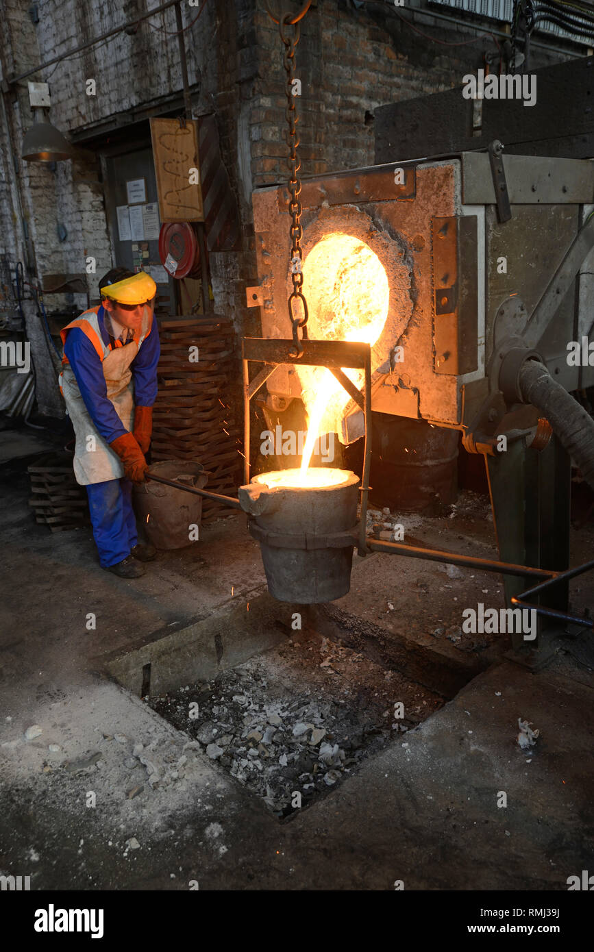 Foundrymen pour ferro fuso dal forno in un ladel. (Shot in luce disponibile con profondità di campo). Foto Stock