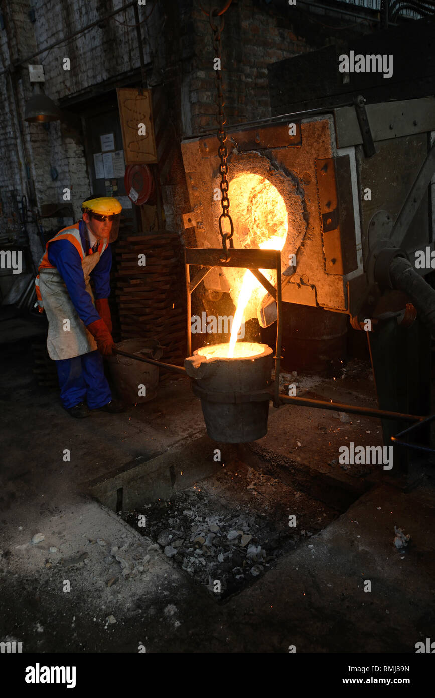 Foundrymen pour ferro fuso dal forno in un ladel. (Shot in luce disponibile con profondità di campo). Foto Stock