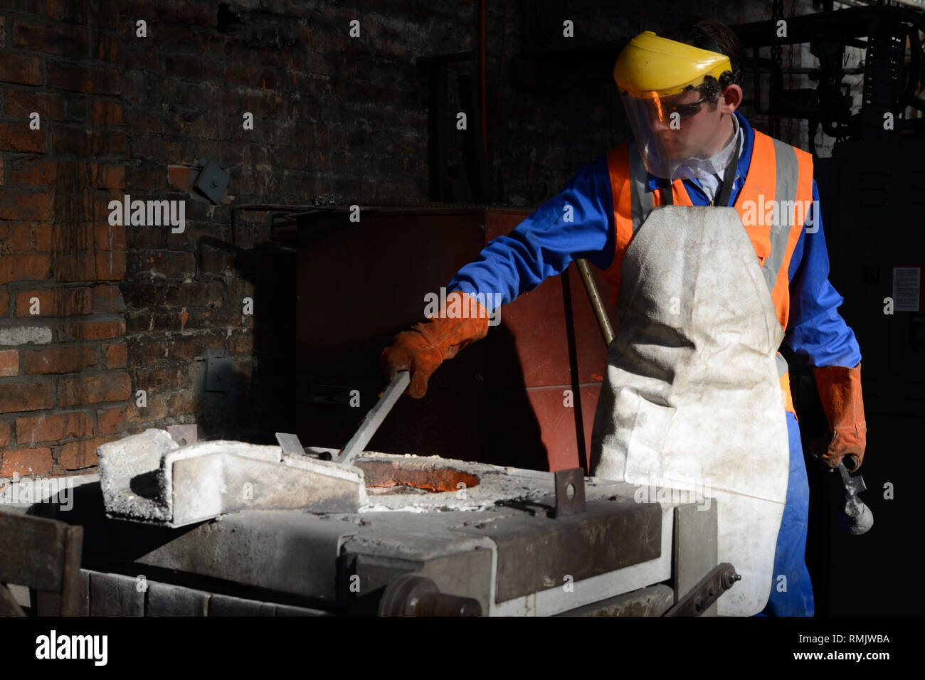 Un fonditore alimenta rottami di metallo in un forno ad induzione per la produzione di ghisa. Foto Stock