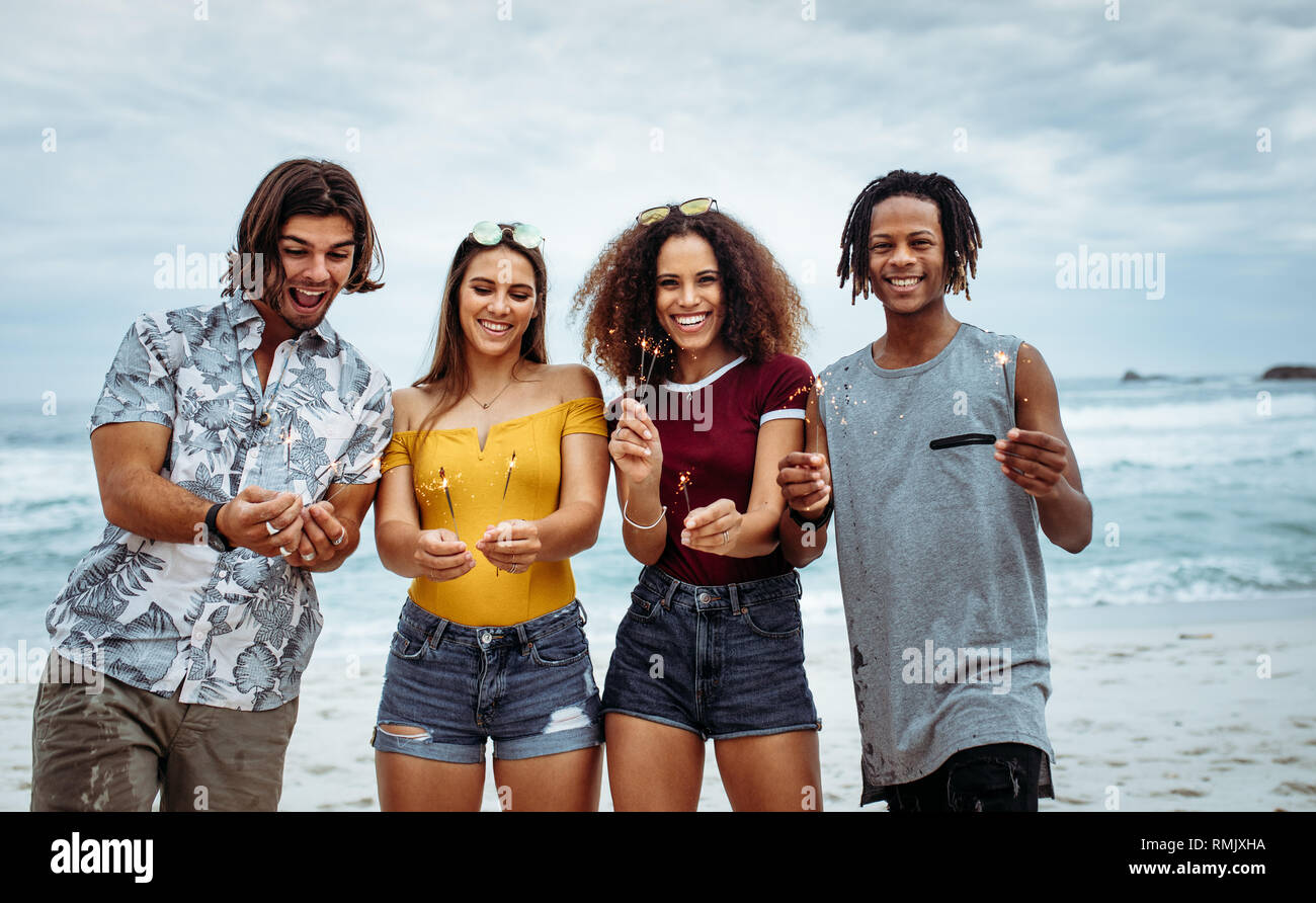 Happy amici festa sulla spiaggia con botti. Multi-etnico gruppo di amici in spiaggia per celebrare il capodanno. Foto Stock