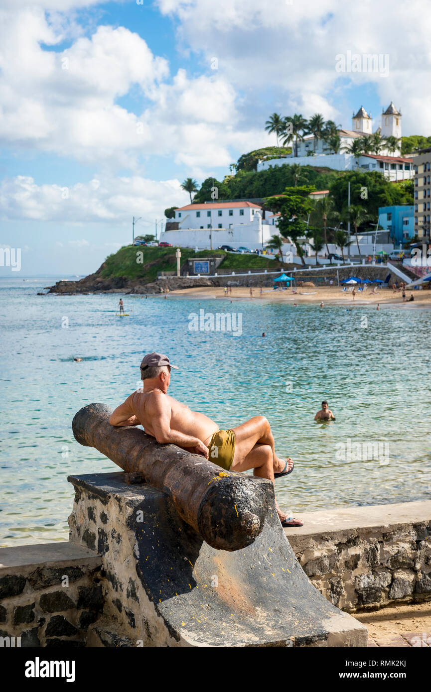 SALVADOR, Brasile - 13 Marzo 2015: un uomo brasiliano si rilassa su uno del cannone reliquie presso il Forte di Santa Maria affacciato sul Porto da Barra Beach. Foto Stock