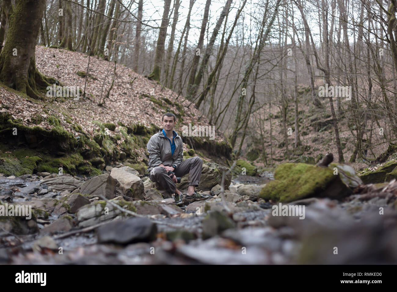 Giovane uomo russo escursionismo in Sochi Parco Nazionale: appoggio seduto su una roccia nei pressi del fiume Foto Stock
