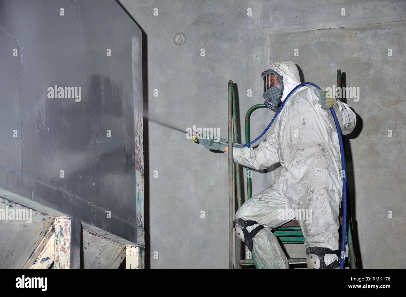 Un trademan utilizza un spruzzo airless a dipingere una tramoggia di carbone all'interno di un impianto di fabbricazione Foto Stock