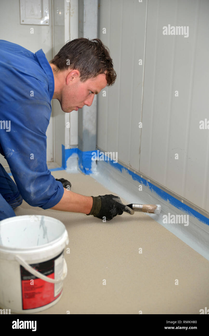 Tradesman pittura bordo del pavimento prima linea prodotto epossidico è utilizzato in un edificio industriale Foto Stock