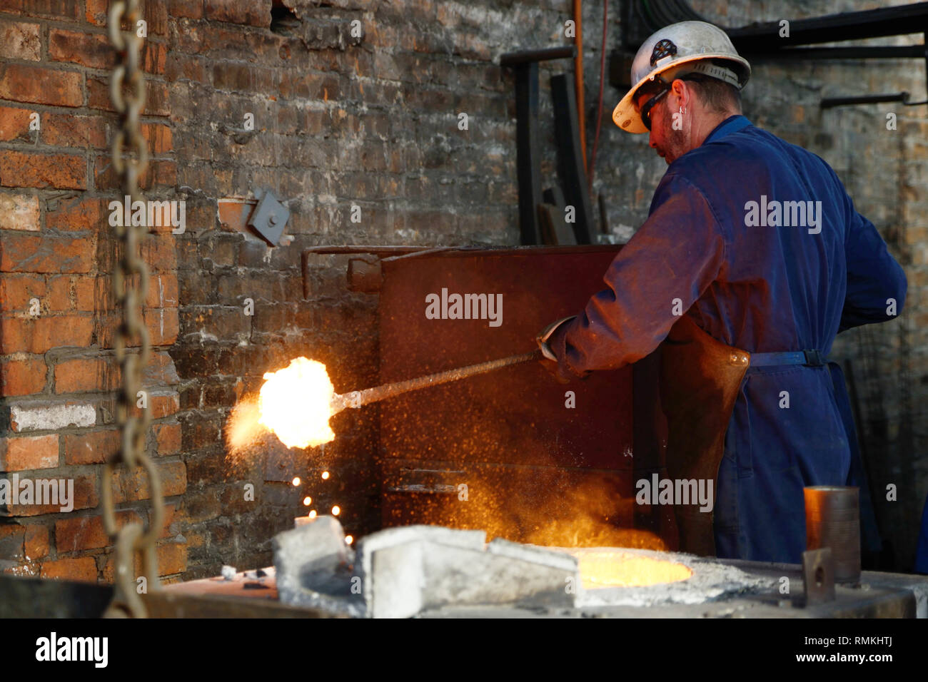 Un fonditore cancella scoria dal ferro fuso nel forno. Foto Stock