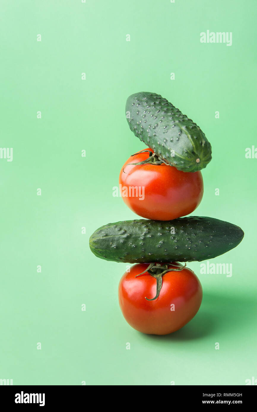 Cumulo di freschi organici grezzi Pomodori Cetrioli impilati uno sull'altro in piramide sul chartreuse lattuga sfondo verde. Equilibrata dieta vegana lif sani Foto Stock