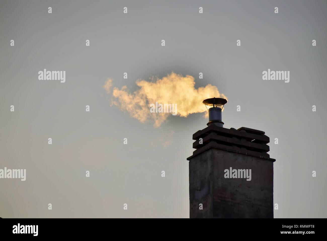Ciminiera di un condominio impianto di riscaldamento. L'inverno raggi del sole al tramonto, il fumo del camino è colorata in giallo. Foto Stock