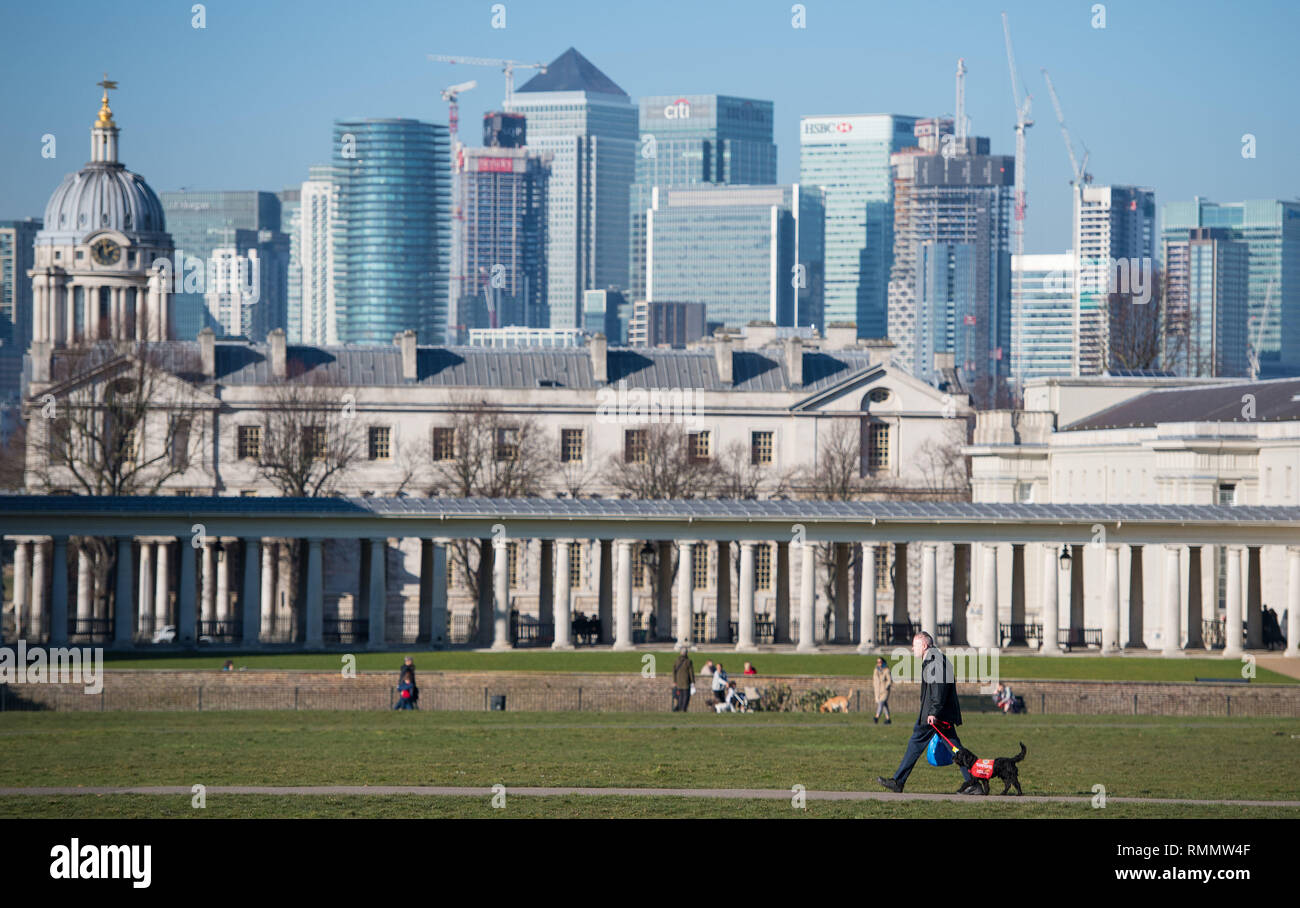 Un uomo cammina il suo cane sotto il sole nel parco di Greenwich, Londra del sud. Forecasters hanno previsto un altro giorno di tempo caldo il venerdì dopo unseasonably clima mite ha visto il più caldo il giorno di San Valentino in più di venti anni il giovedì con un massimo di 16.1C (61F) registrate nella cittadina gallese di Bala, Gwynedd. Foto Stock