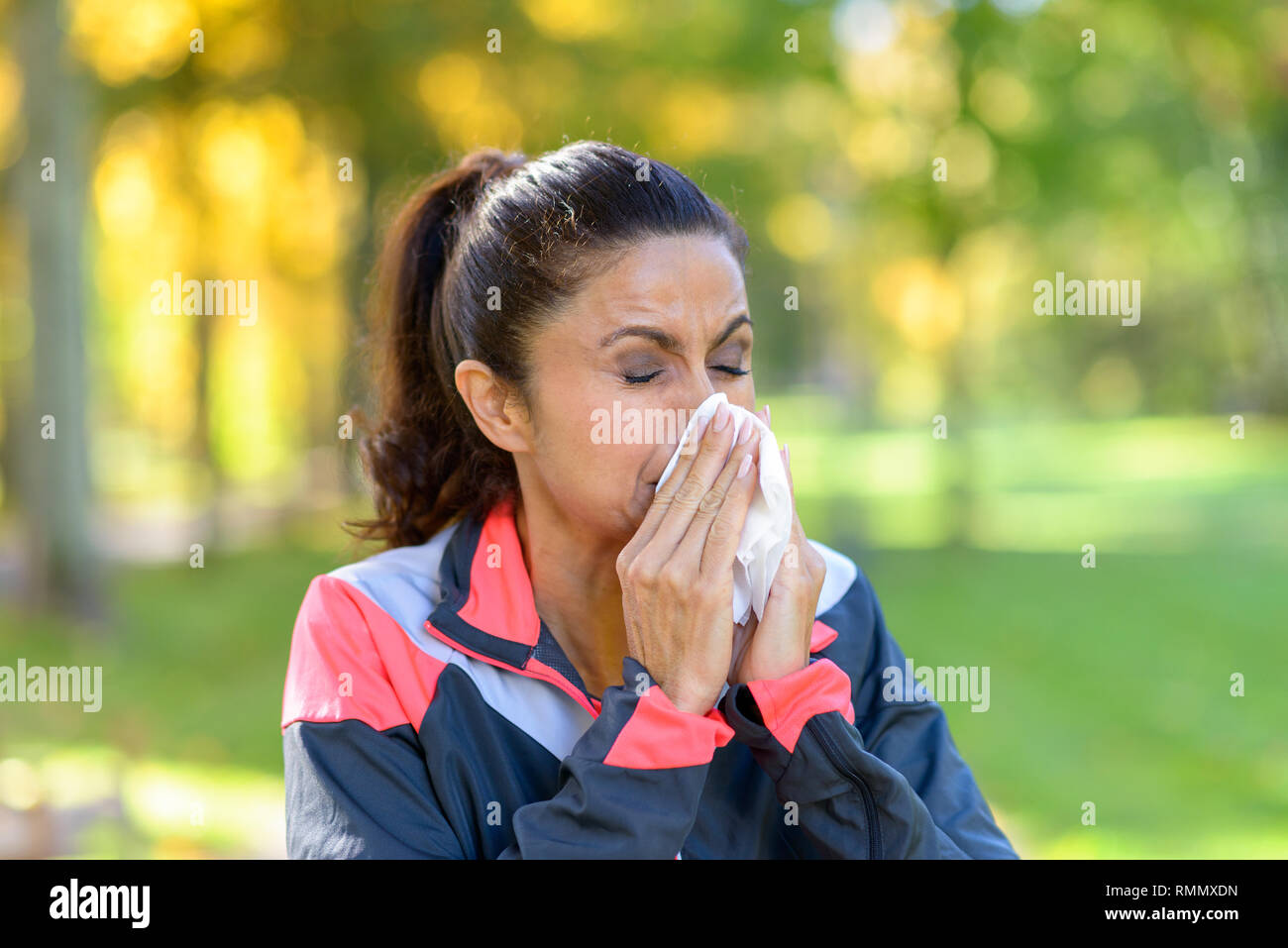 Donna soffia il naso su un tessuto esterno in una verdeggiante parco verde mentre jogging concettuale del l'influenza stagionale o allergie Foto Stock