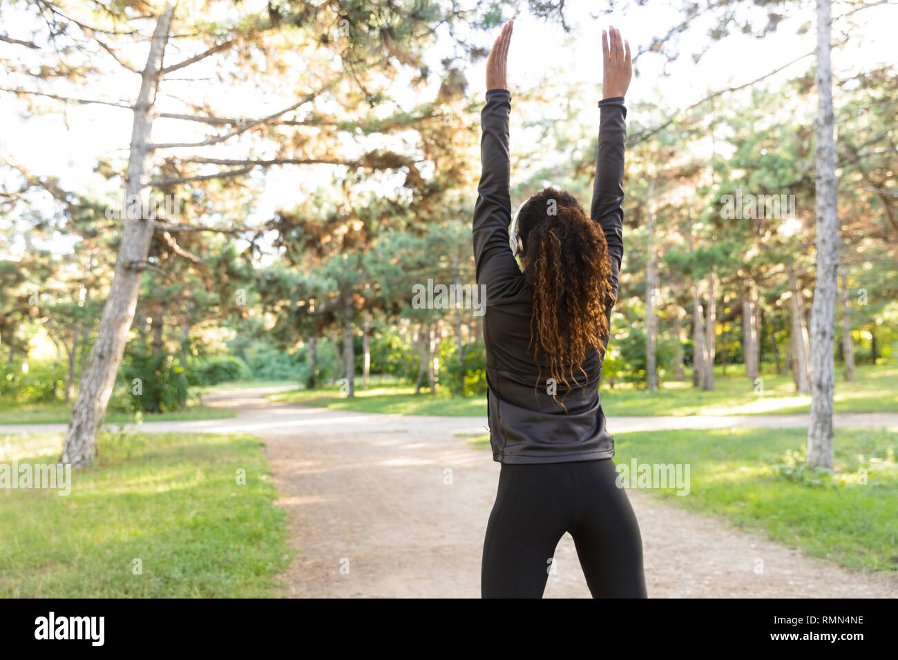 Immagine della donna skinny 20s indossare tuta nera che lavora fuori e stretching corpo nel parco verde Foto Stock