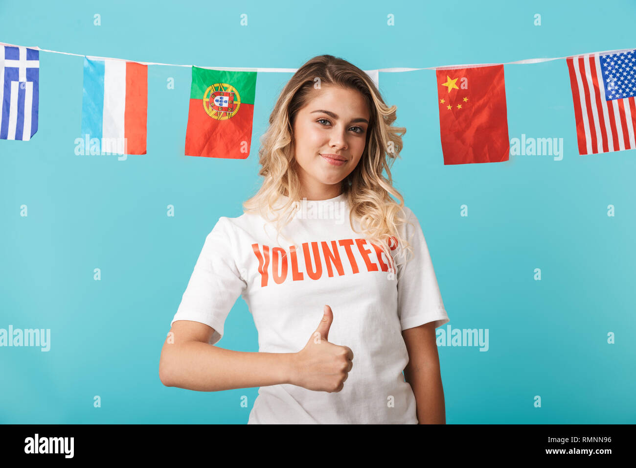 Ritratto di un sorridente ragazza voluteer indossa la t-shirt in piedi isolato su sfondo blu, mostrando pollice in alto Foto Stock