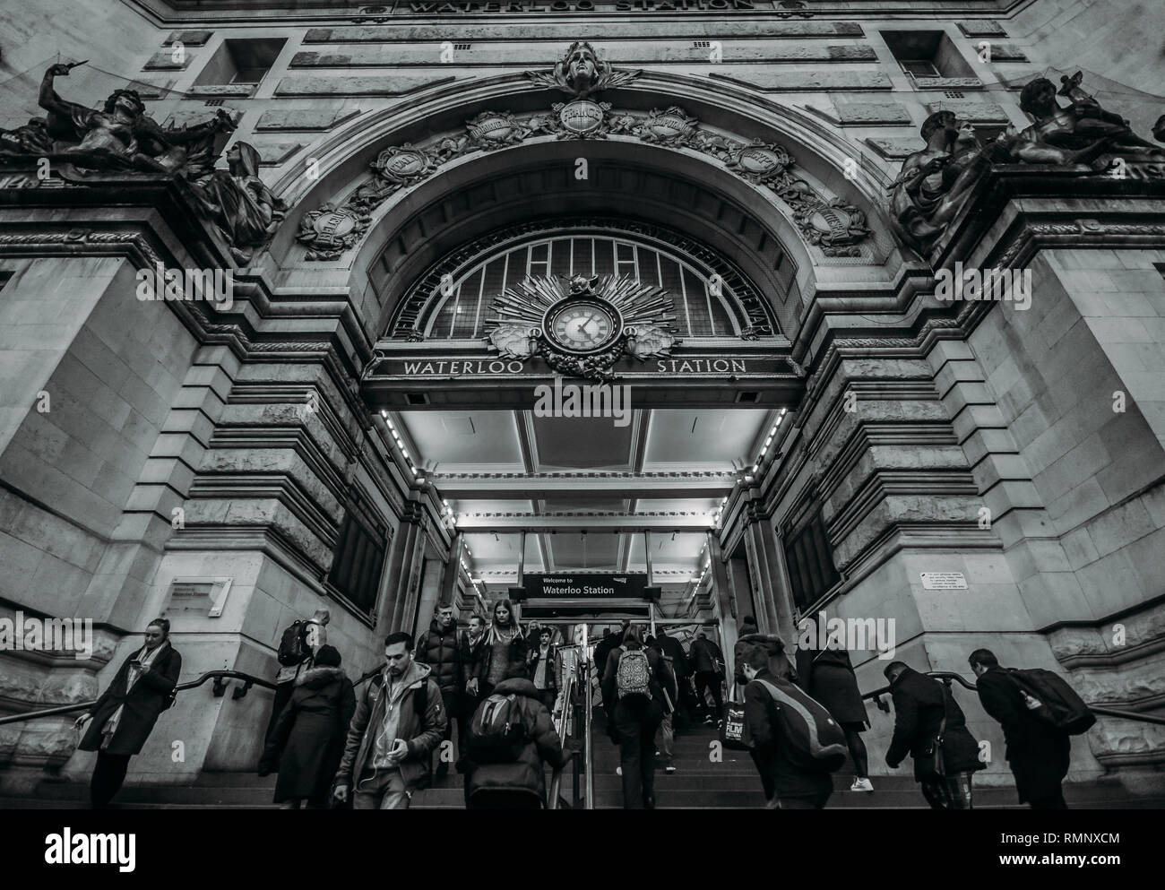 London, Regno Unito - Feb 12, 2019: pendolari passando attraverso l'ingresso della stazione ferroviaria di Waterloo in ora di punta, uno dei più grandi di Londra - monocromatico Foto Stock