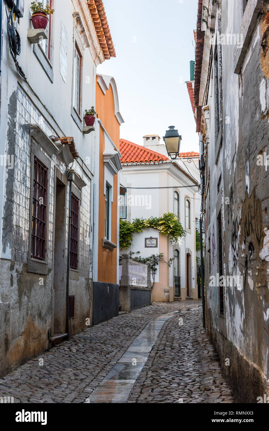 Avvolgimento acciottolato stretto vicolo che conduce lontano tra tradizionale fatiscente e rinnovato imbiancato case di pietra in Cascais Portogallo Foto Stock