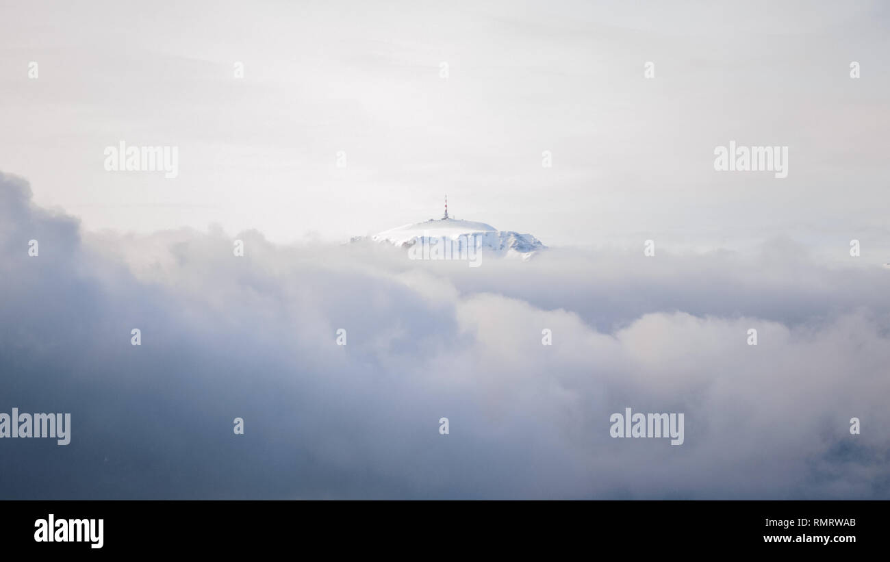 Picco di montagna con un TV/radio relè sulla parte superiore, come si è visto sopra le nuvole, su un nuvoloso giorno di inverno con inversione atmosferica - Costila nelle montagne di Bucegi, Foto Stock