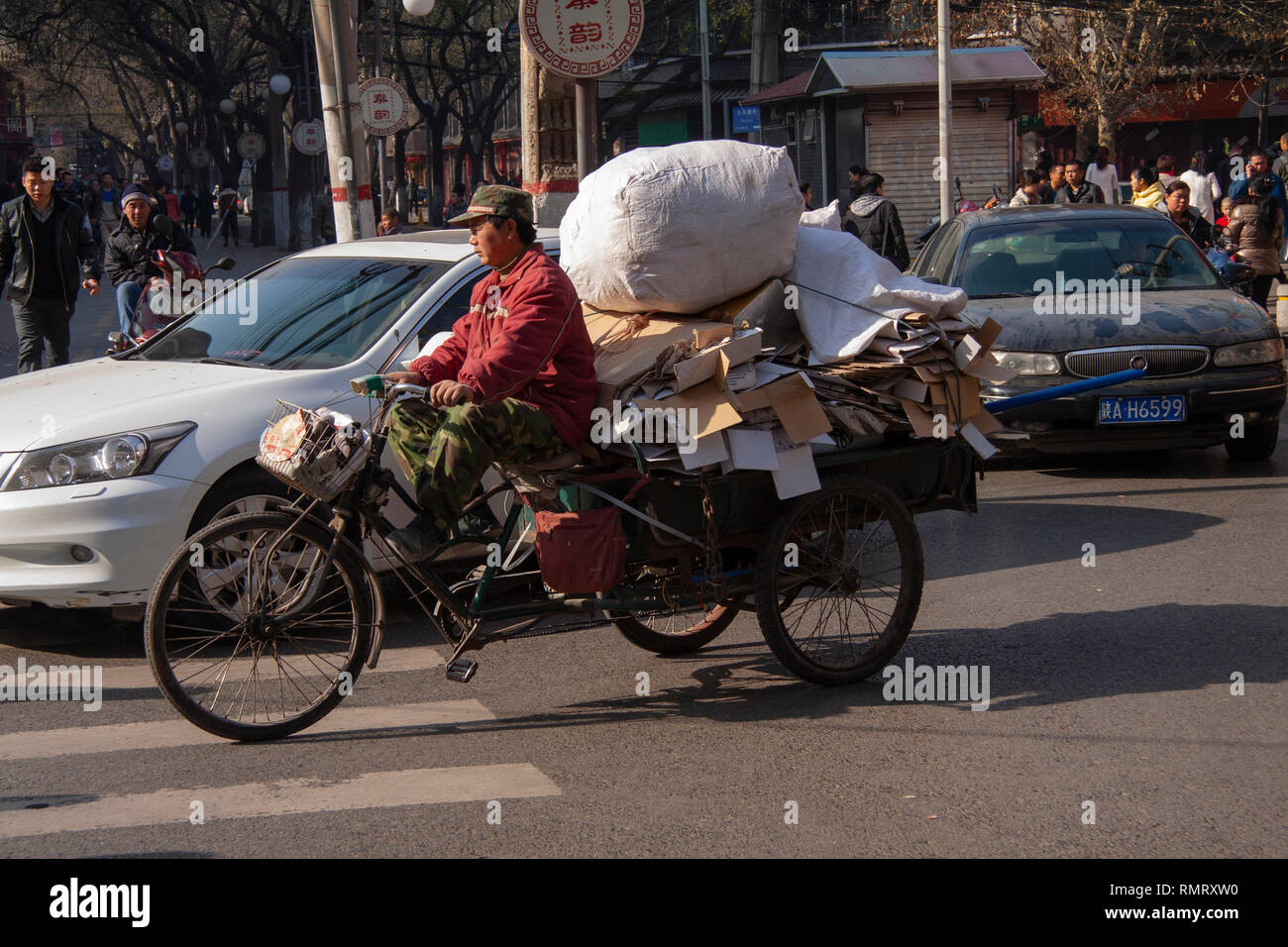 Uomo cinese a cavallo di un triciclo cargo caricata di beni in una strada a Pechino in Cina. Il carico di biciclette e tricicli di nolo sono popolari trasporto in Cina. Foto Stock