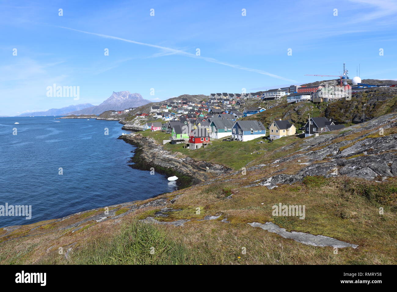 Nuuk, capitale della Groenlandia. Città in Groenlandia con case colorate sulla riva della baia blu dove galleggia un iceberg Foto Stock