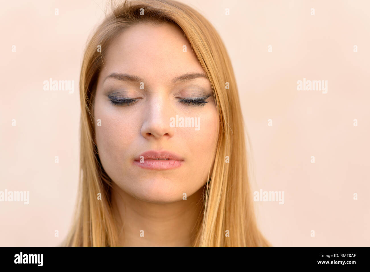 Serena attraente donna bionda con gli occhi chiusi rilassante, de-sollecitazione o meditando in una chiusura colpo alla testa ritratto su una posizione neutra di studio backgro Foto Stock