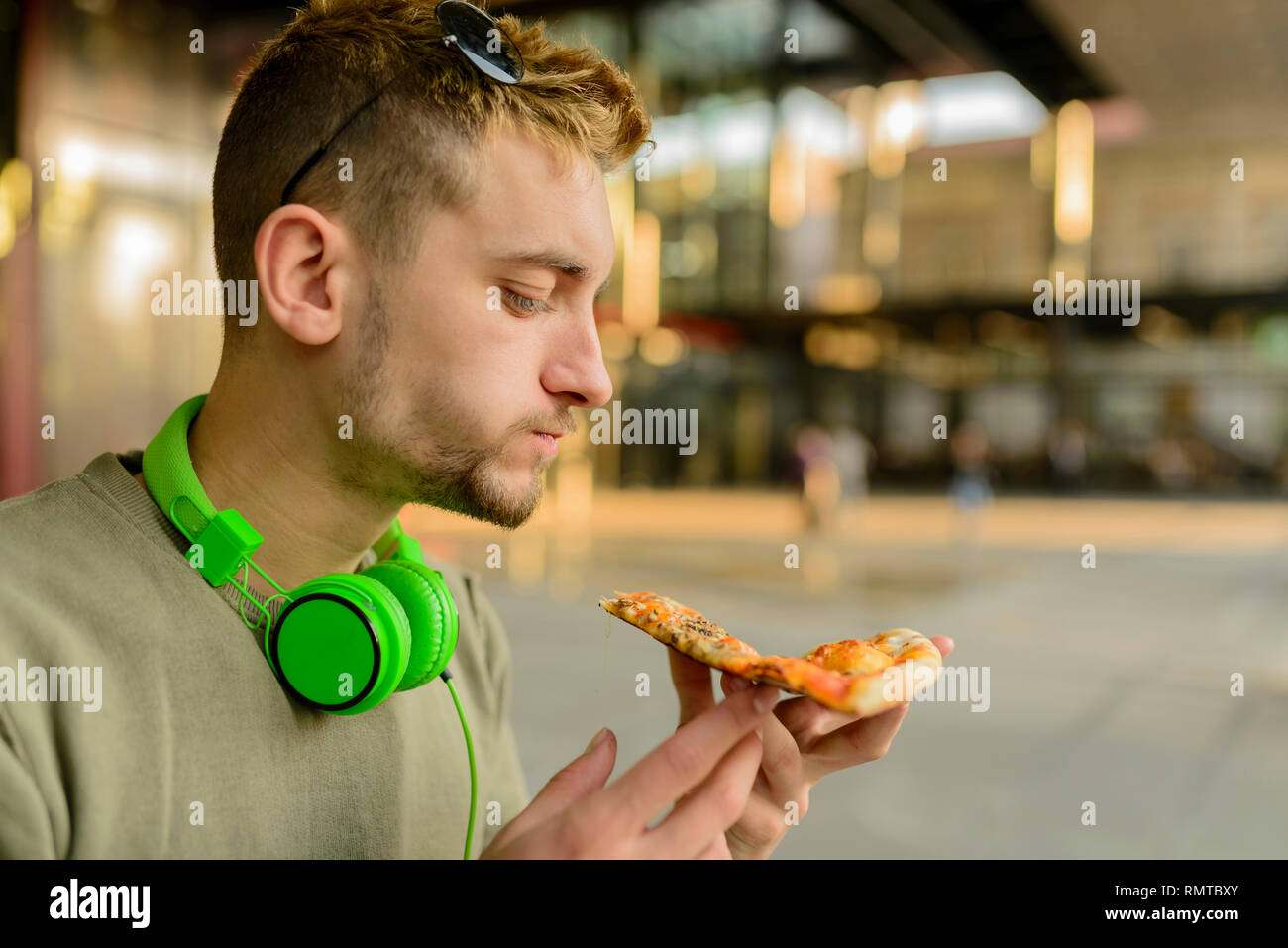 Bel giovane con le cuffie a mangiare la pizza in strada di città Foto Stock