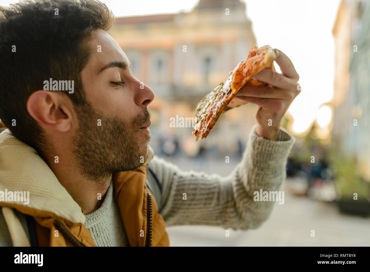 Bello barbuto giovane con camicia arancione di mangiare la pizza in strada di città Foto Stock