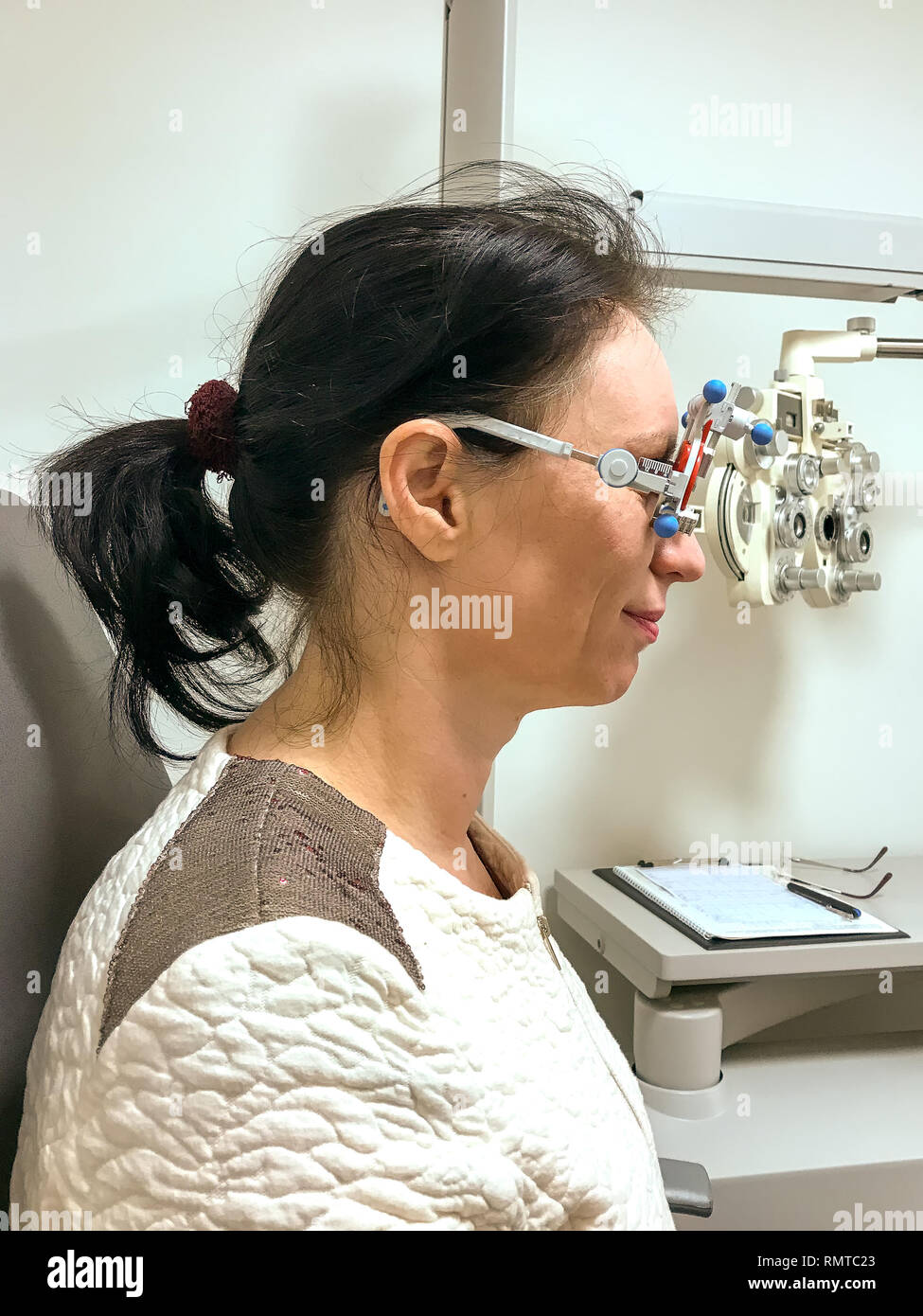 La donna che viene testato per nuovi occhiali a un all'ottico optometrista utilizzando attrezzature intercambiabili con lenti correttive per misurare la sua acuity Foto Stock