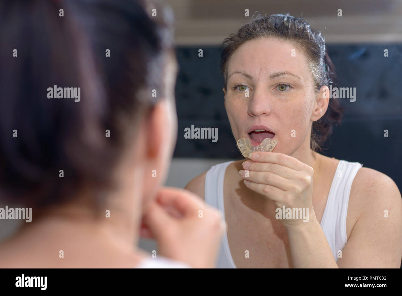 Donna che mantiene un morso superiore piastra per impedire la macinazione i suoi denti insieme come si guarda la sua immagine nello specchio Foto Stock