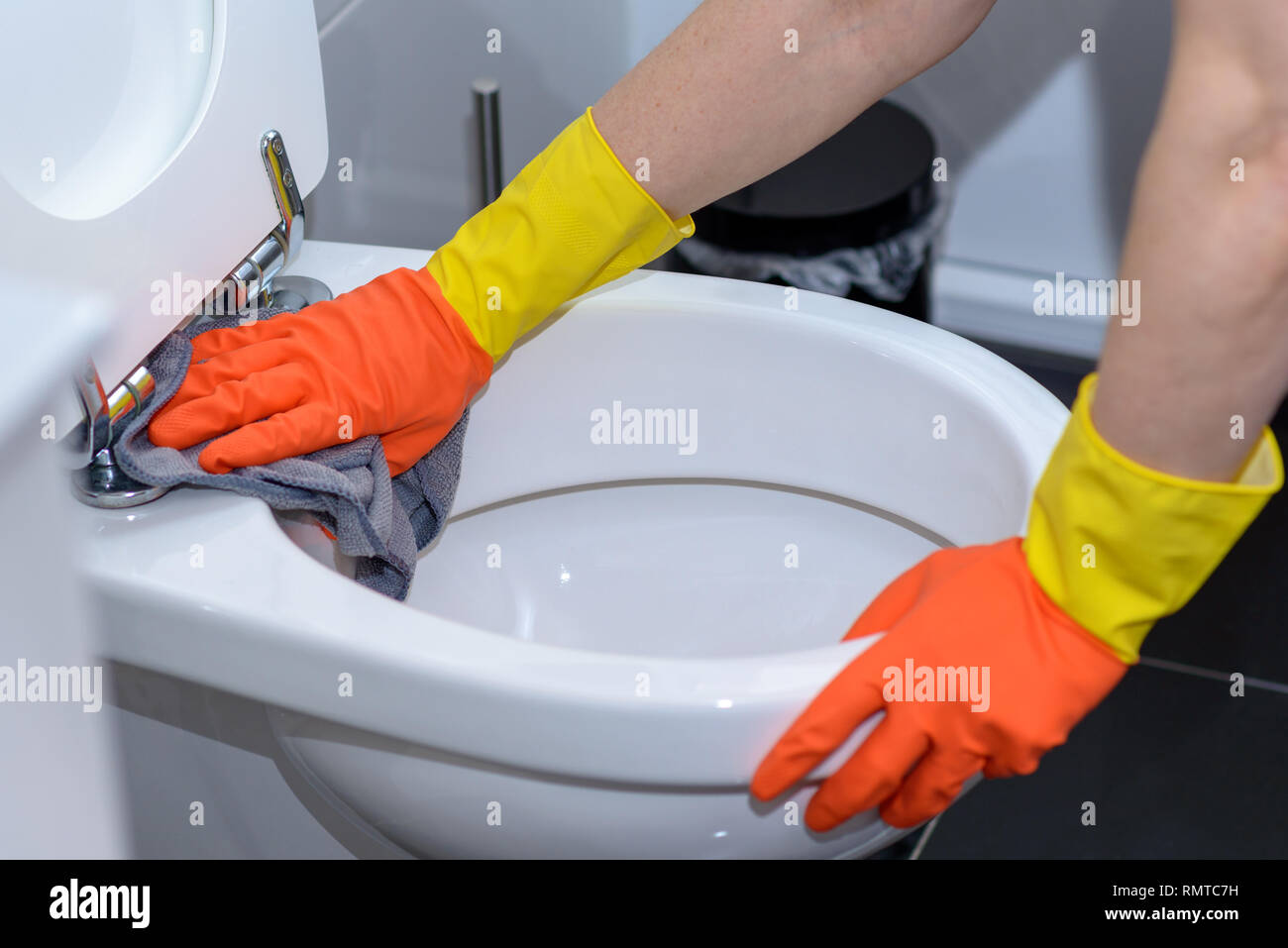 Persona che indossa l'arancione guanti di gomma tergi fuori una tazza igienica con un panno in faccende di casa e concetto di igiene Foto Stock