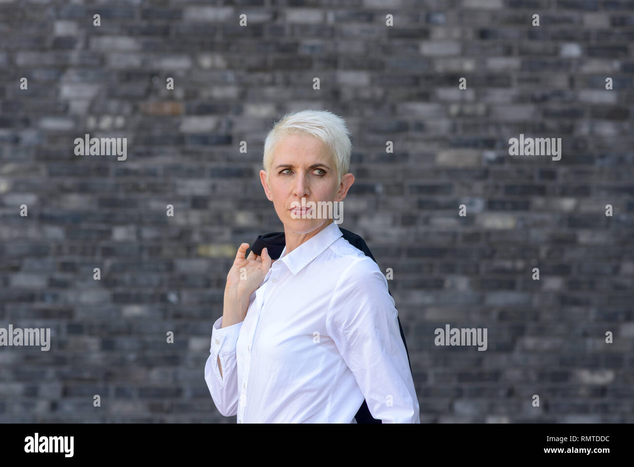 La donna indossa la sua giacca sulle sue spalle davanti ad un muro nero Foto Stock