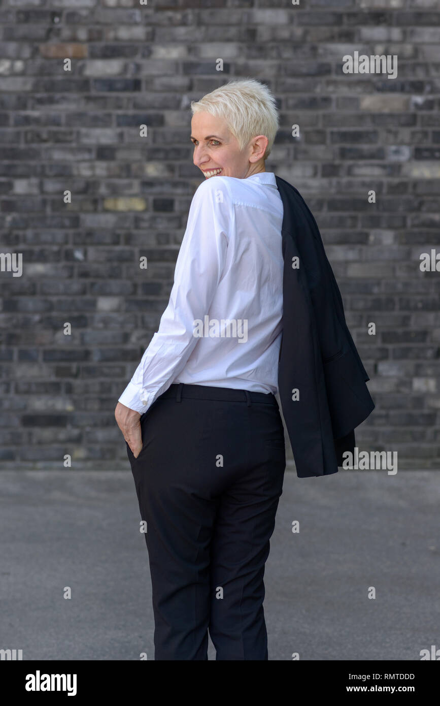 Felice è la donna che indossa la sua giacca sulle sue spalle davanti ad un muro nero Foto Stock