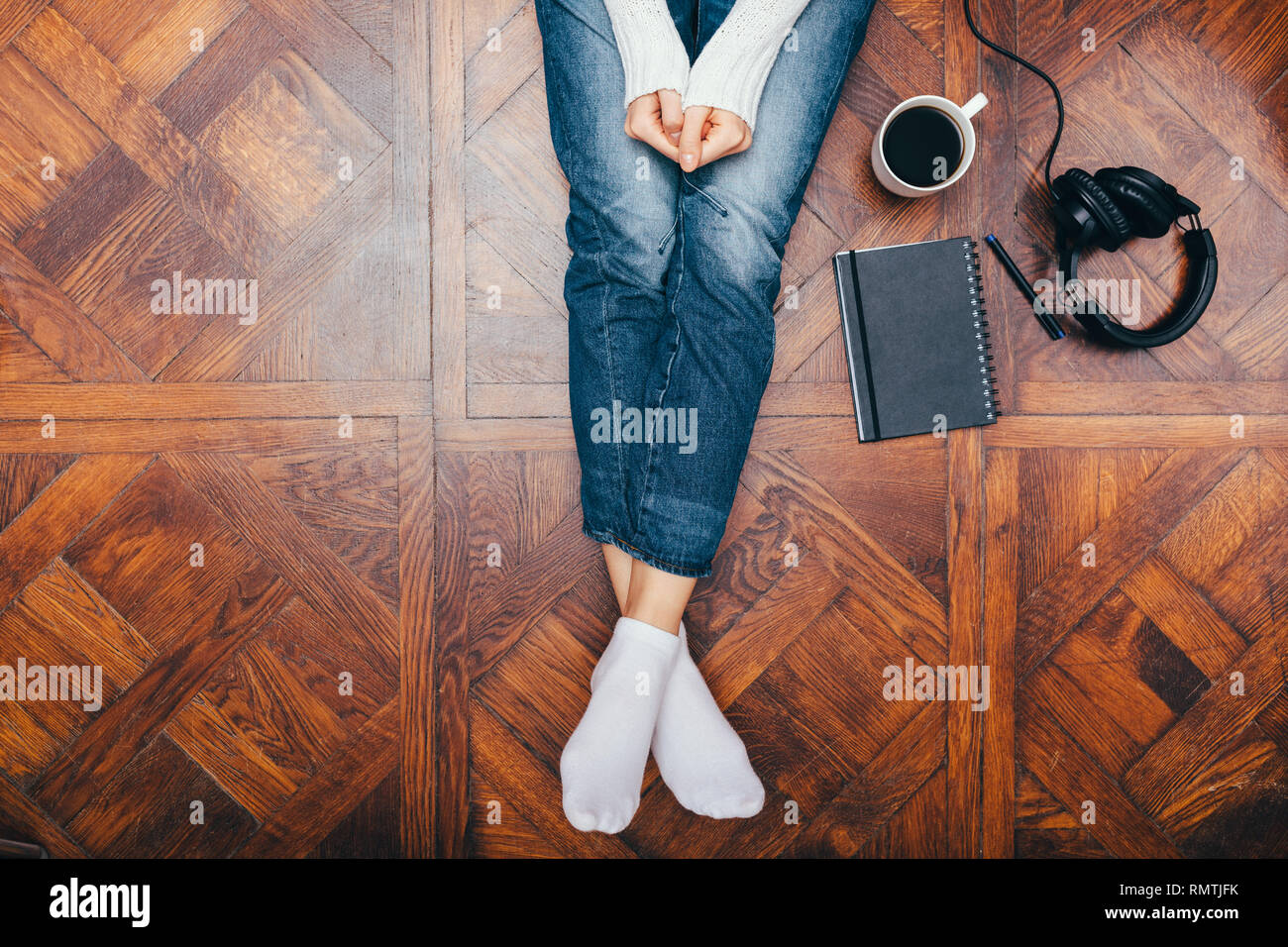 Close-up giovani femmine per le gambe in jeans su pavimento di legno a casa  nei pressi di notepad, una tazza di caffè e cuffie, vista dall'alto Foto  stock - Alamy