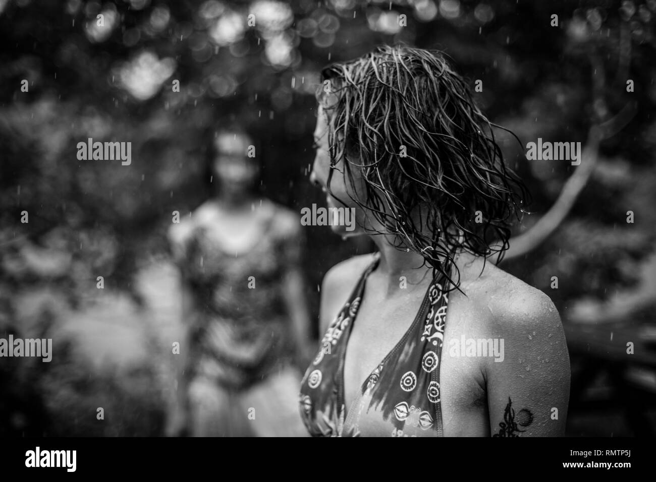 Donna in piedi sotto la pioggia in un costume da bagno guardando dietro di lei a una donna sfocate, in bianco e nero Foto Stock